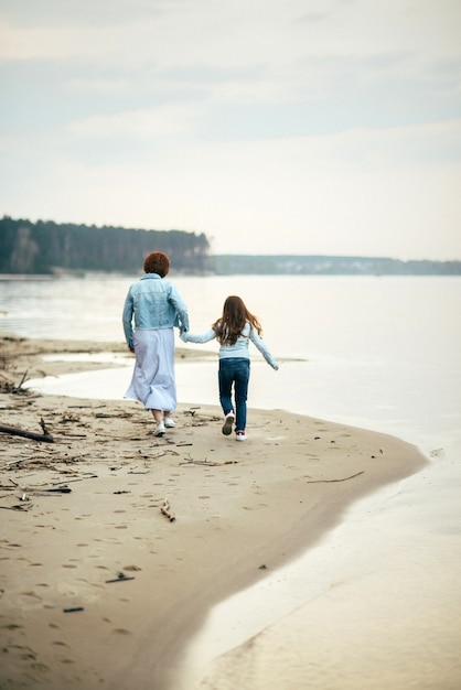 Madre e hija pequeña caminan juntas por la orilla del mar cogidos de la mano