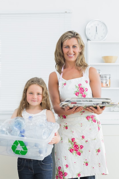 Foto madre e hija de pie en la cocina con los residuos para el reciclaje