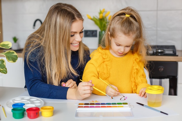 Madre e hija pintando en casa. Niño divirtiéndose. Educación infantil, ocio preescolar