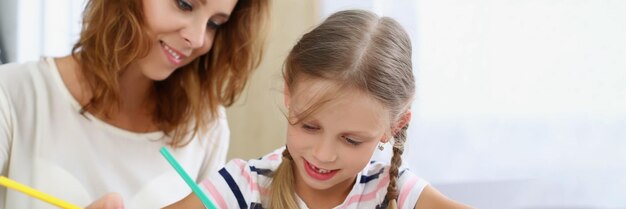 Madre e hija pintando con lápices en álbum tiempo feliz con niño