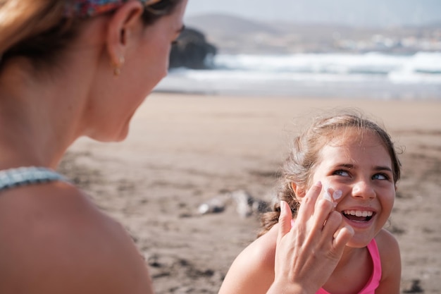 Madre e hija poniéndose protector solar en un soleado día de playa Concepto de crema solar divertida