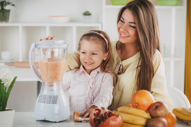 Madre e hija preparando bebida de frutas saludables o comida en una licuadora en la cocina.