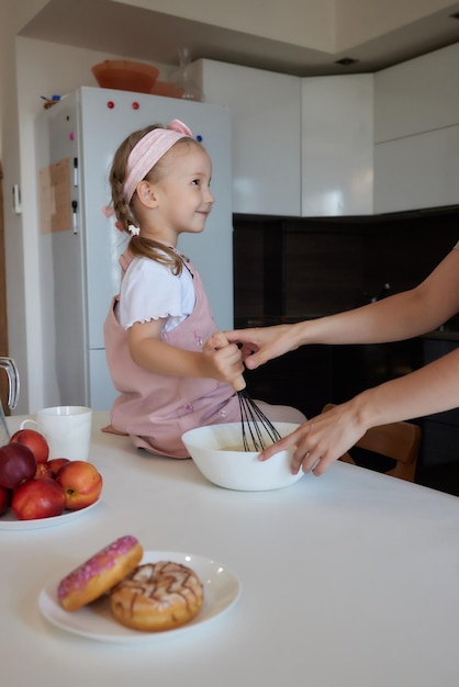 Madre e hija preparando un pastel dulce con leche de harina sentadas en sillas en una mesa en un moderno