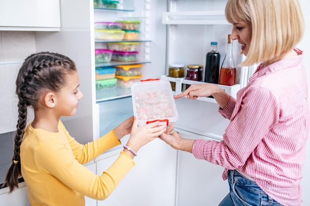 Madre e hija preparando verduras juntas para el invierno en recipientes al vacío.