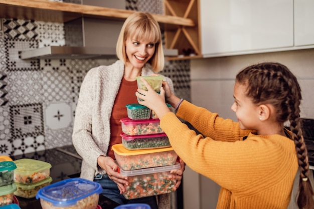 Madre e hija preparando verduras juntas para el invierno en recipientes al vacío.