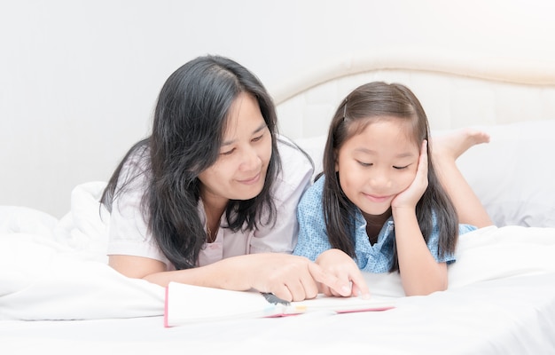 Madre e hija que leen el libro en la cama, educación del concepto