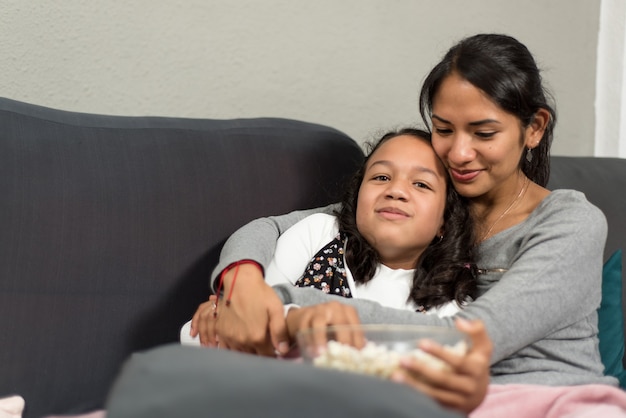 Madre e hija relajadas en casa. Comiendo palomitas y viendo series en el sofá.