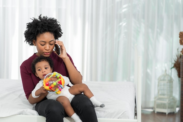 Foto madre e hija en la sala de estar una madre africana está ocupada haciendo llamadas telefónicas y cuidando a sus hijos mientras trabaja desde casa