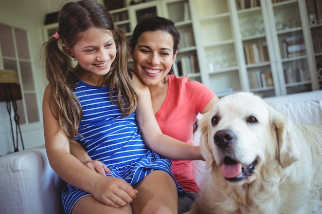 Madre e hija sentada con un perro mascota en la sala de estar