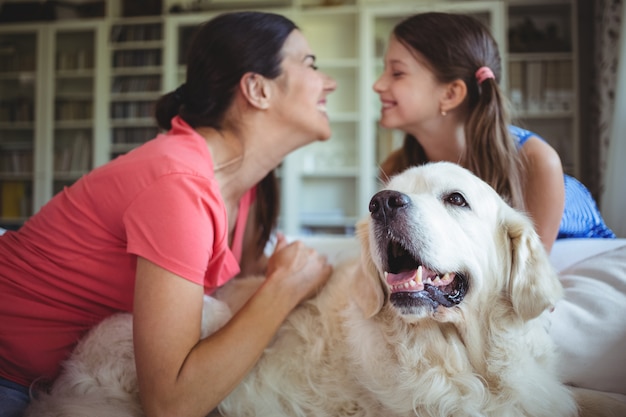 Madre e hija sentada con un perro mascota en la sala de estar