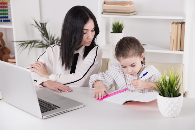 Madre e hija sentadas con la computadora juntas en el escritorio