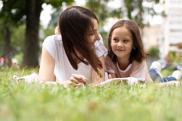 Madre e hija sentadas juntas sobre hierba verde. Madre e hija teniendo una conversación divertida.