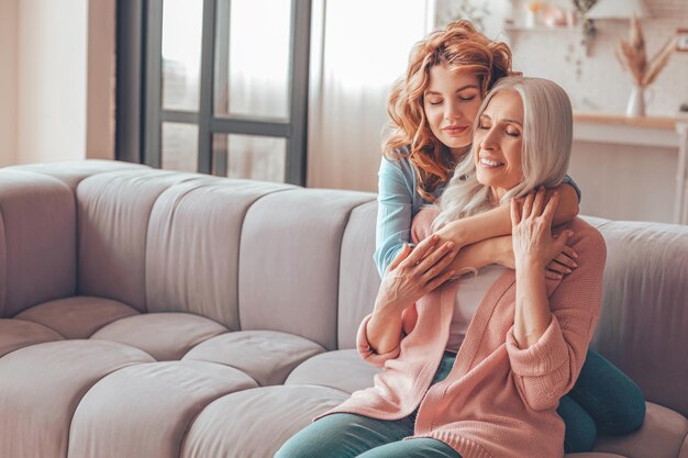 Madre e hija sentadas en el sofá y abrazándose