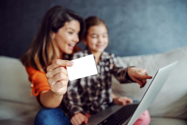 Madre e hija sentadas en el sofá y usando una computadora portátil para comprar en línea