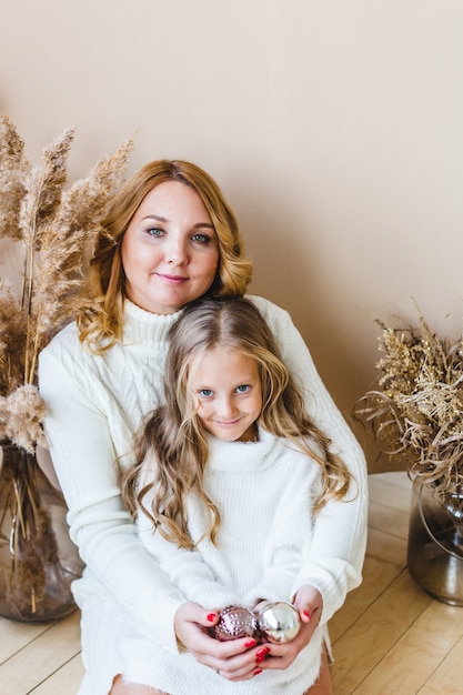 Madre e hija sentadas y sosteniendo adornos navideños