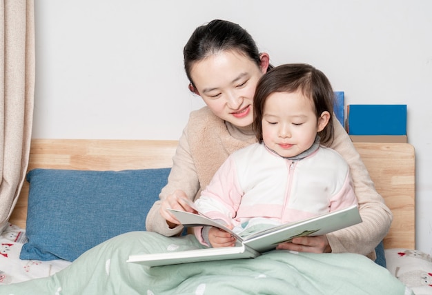 Madre e hija se sientan en la cama leyendo juntas