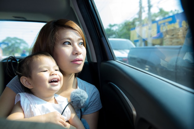 Madre e hija se sientan juntas en el asiento trasero del auto mirando por la ventana.