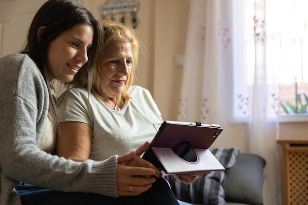 Madre e hija en el sofá de casa mientras miran la tableta y son felices