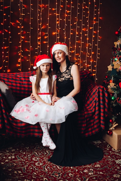 Madre e hija en el sombrero de Santa Claus contra la iluminación guirnalda.