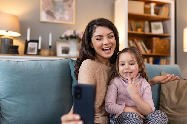 Madre e hija sonrientes en una videollamada usando teléfono digital en casa mientras hacen una videollama y saludan sentadas en el sofá Mujer y su lindo niño haciendo una videoconferencia con los abuelos
