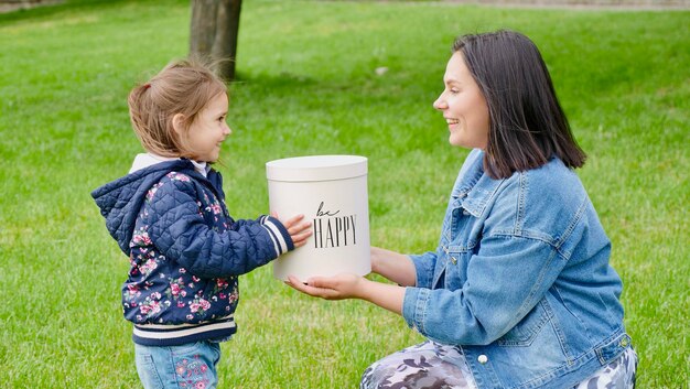 Madre e hija sosteniendo una caja de regalo con la inscripción Sé feliz de cerca sin rostro Madre con bebé afuera