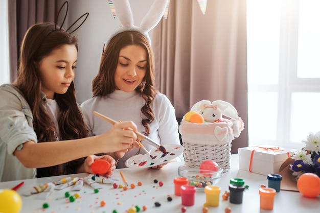 Madre e hija sostienen pinceles y obtienen un poco de color para los huevos.