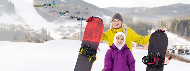 madre e hija con tablas de snowboard en el resort de invierno