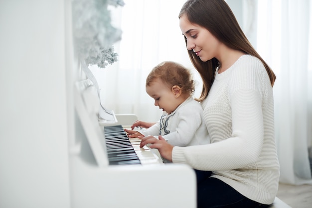 Madre e hija tocando el piano blanco, cerca wiew