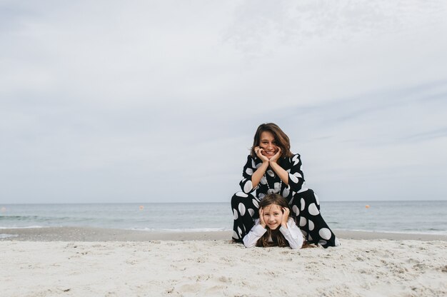 Madre e hija tomados de la mano y caminando en la playa.