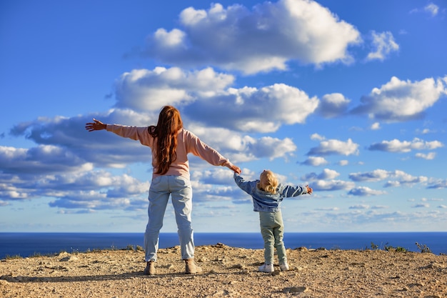 Foto madre e hija tomados de la mano y mirando hacia arriba admirando las increíbles nubes sobre el mar viajar c