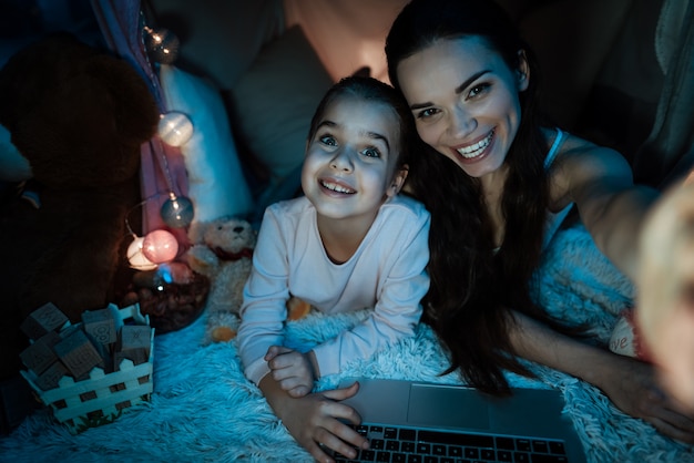 Madre e hija tomando selfie en casa de almohadas.