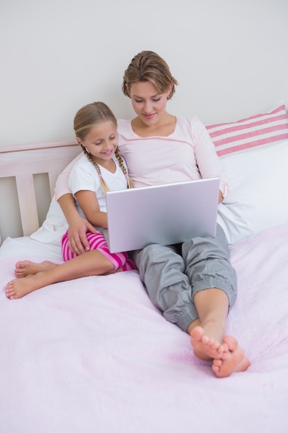 Madre e hija usando la computadora portátil en la cama