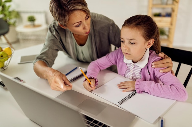 Madre e hija usando una computadora portátil mientras estudian en casa