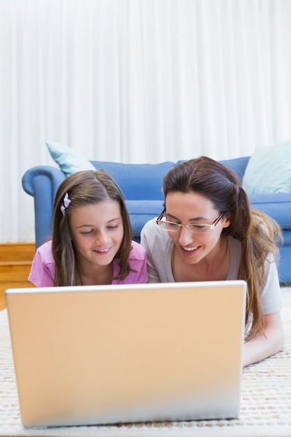 Madre e hija usando la computadora portátil en el piso