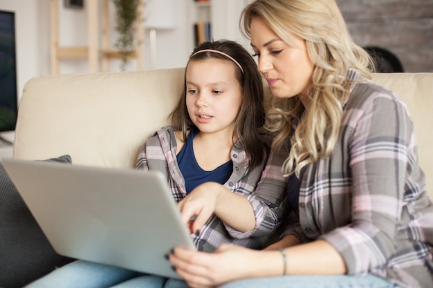 Madre e hija usando una computadora portátil con tecnología inalámbrica para navegar en internet.