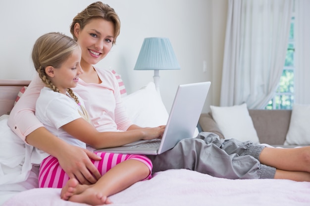 Madre e hija usando laptop en la cama