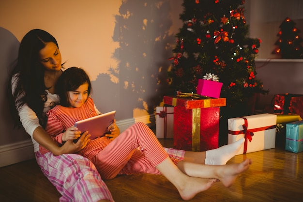 Madre e hija usando tableta al lado del árbol de Navidad