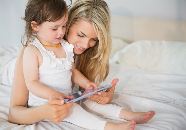 Madre e hija usando tableta digital en la cama