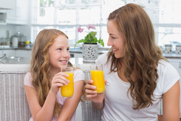 Madre e hija con vasos de jugo de naranja en la cocina