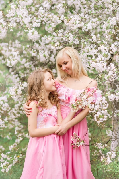 Madre e hija en vestidos de color rosa en un jardín floreciente en primavera.