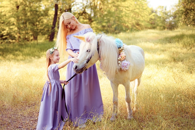 Madre e hija con vestidos de lavanda similares están acariciando a un unicornio