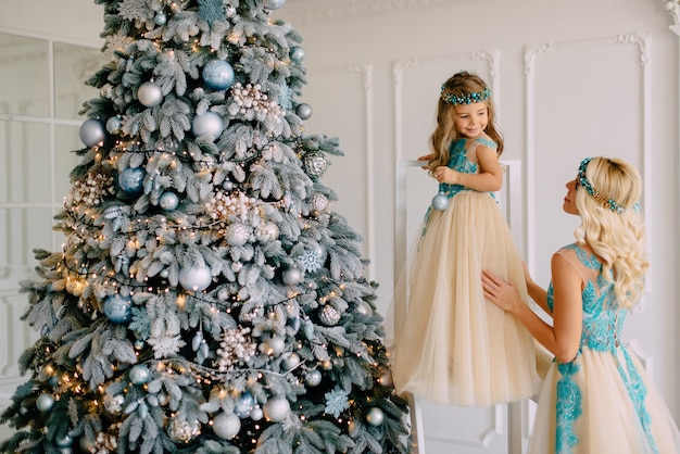 Madre e hija en vestidos de lujo decoran el árbol de Navidad