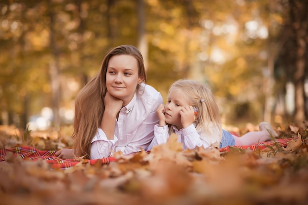 Madre e hija yacen en el parque en el follaje de otoño