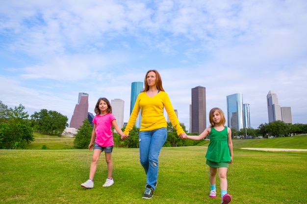 Madre e hijas caminando tomados de la mano en el horizonte de la ciudad