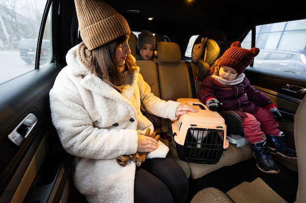 Madre e hijas con carro de jaula de plástico de viaje de gato en coche