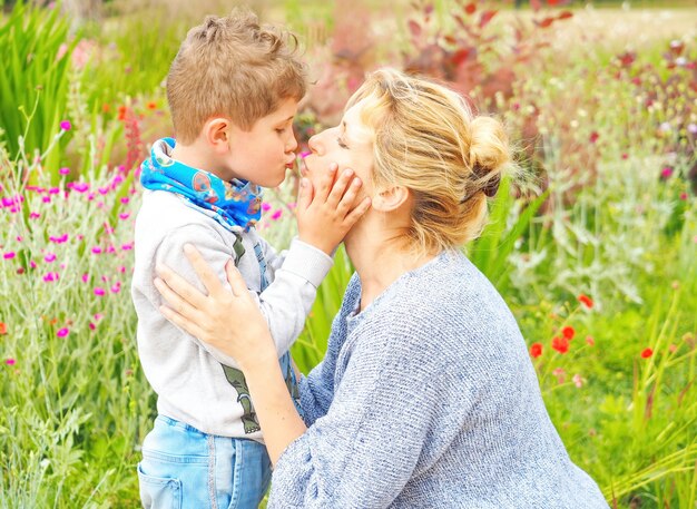 Madre e hijo se abrazan y besan en el jardín con flores.