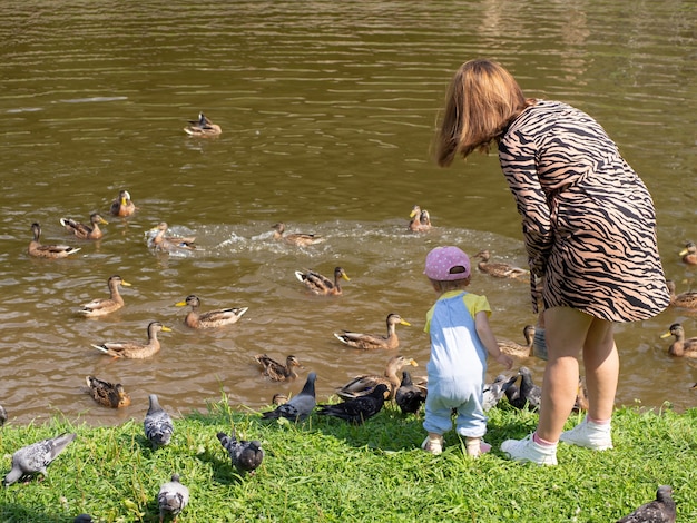 Madre e hijo alimentan a los pájaros en la orilla del lago de la ciudad.