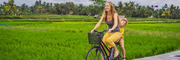 Madre e hijo andan en bicicleta en un campo de arroz en ubud bali viajan a bali con banner de concepto de niños