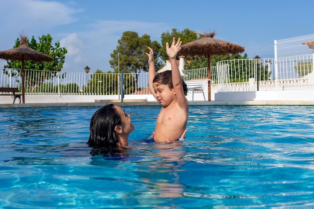 Madre e hijo bañándose en la piscina, ambos sonriendo felizmente mirando el uno al otro mientras disfrutan