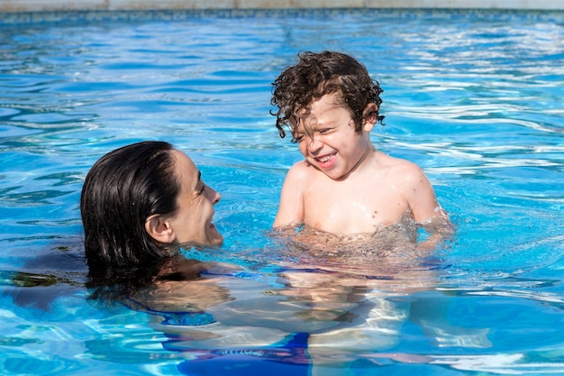 Madre e hijo bañándose en la piscina, ambos sonriendo felizmente mirando el uno al otro mientras disfrutan